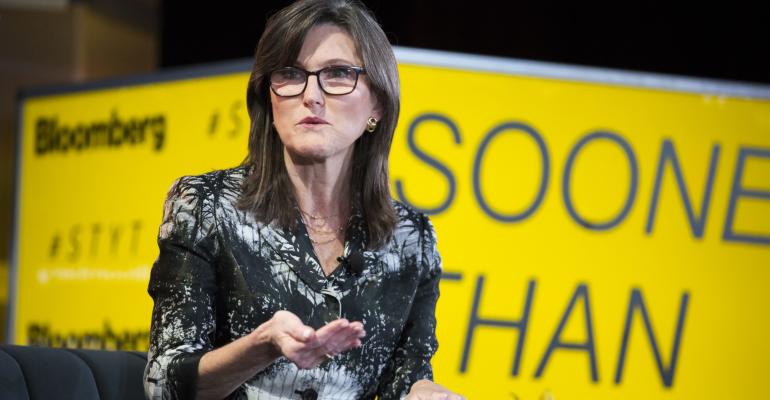 Image of investor Cathie Wood in front of yellow background. She is gesturing and speaking at an event.