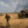 Israeli soldiers stand near their tank while smoke due to airstrikes and shelling rises from the Gaza Strip